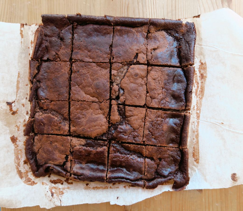 Heather's take on Boo's Ridiculous(ly low calorie) Brownie with a shiny, crinkled crust created using erythritol as a sweetener in place of sugar. Bird's eye shot on parchment paper on a wooden stool as backdrop :)
